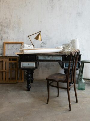 A rustic art studio featuring a vintage desk, wooden chair, and abstract frames on a textured wall.