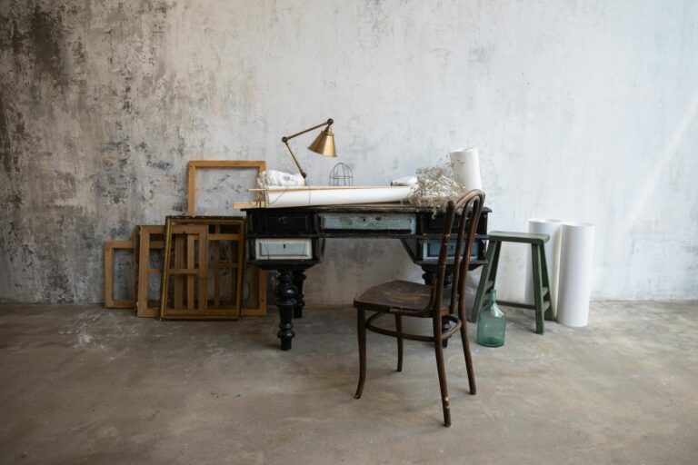 A rustic art studio featuring a vintage desk, wooden chair, and abstract frames on a textured wall.